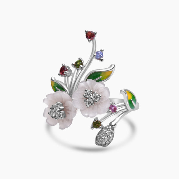 A silver cocktail ring with a design of mother of pearl flowers, zircon stones, green and yellow enamel leaves, and silver flower buds.