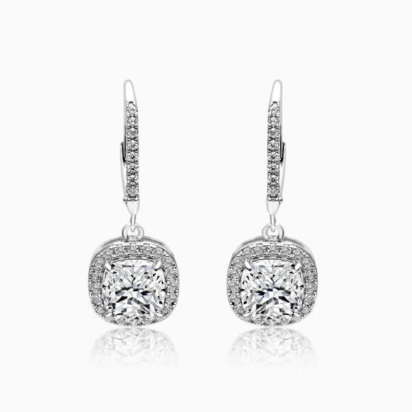 A pair of silver dangling grand solitaire earrings with a central cubic zirconia surrounded by smaller zirconia crystals, attached to silver hooks.