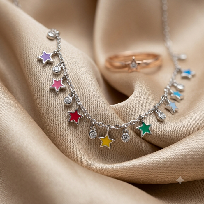 A silver-toned star charm necklace with colorful enamel star pendants in purple, pink, red, yellow, green, and blue, displayed on draped champagne satin fabric next to a rose gold ring.