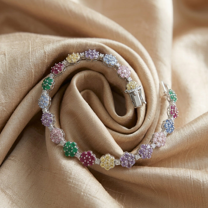 A silver-toned bracelet with colorful gemstone flower clusters, displayed on a draped beige silk fabric.