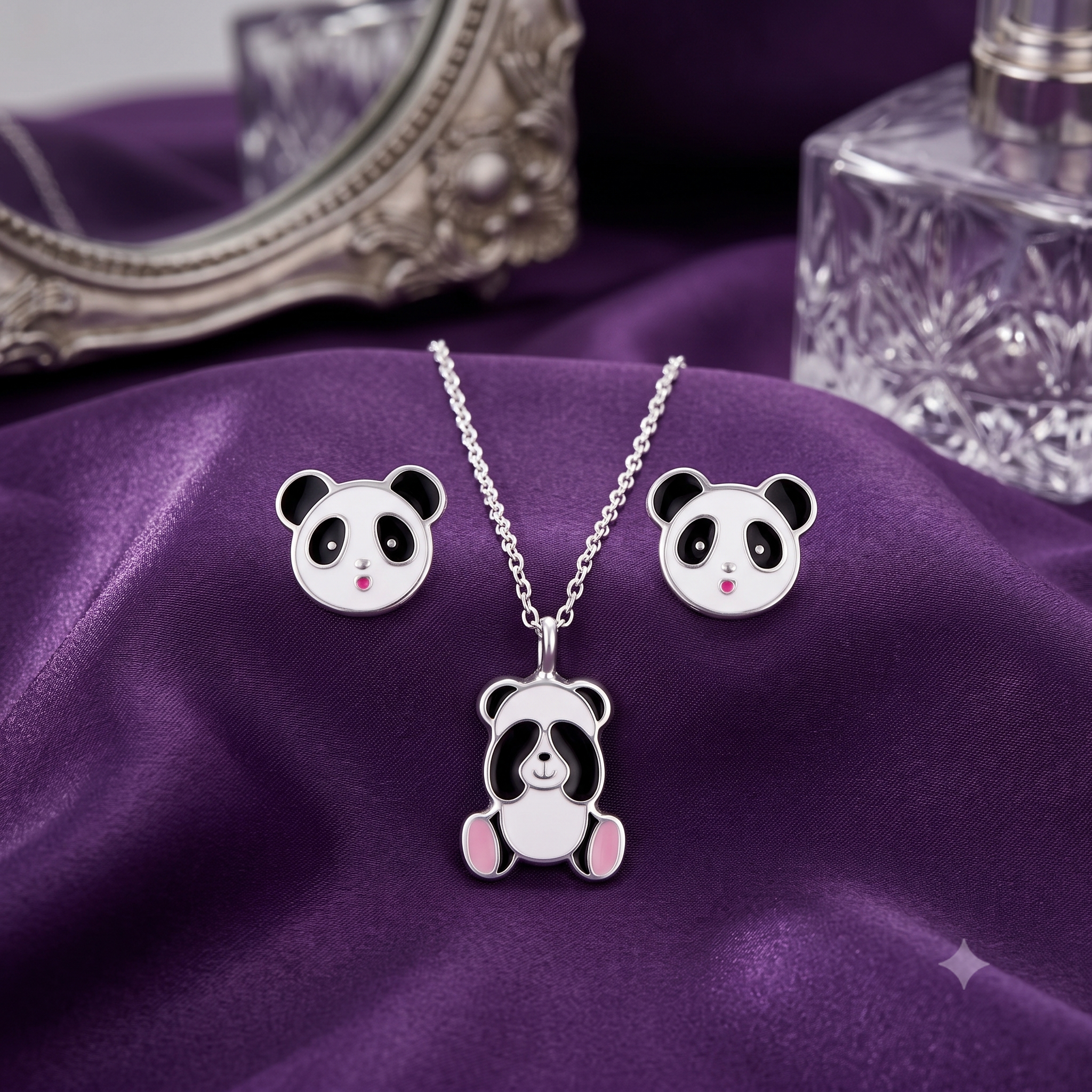 A silver-toned panda-themed jewelry set featuring a necklace with a seated panda pendant and matching stud earrings, displayed on draped purple fabric with decorative props in the background.