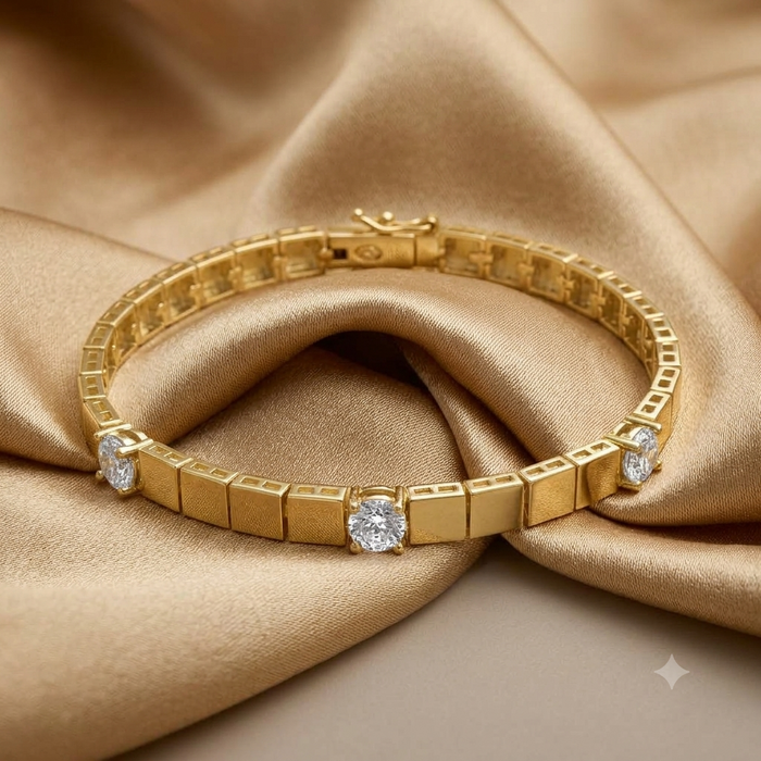 A gold tennis bracelet with round-cut clear gemstones, displayed on draped champagne-colored satin fabric.