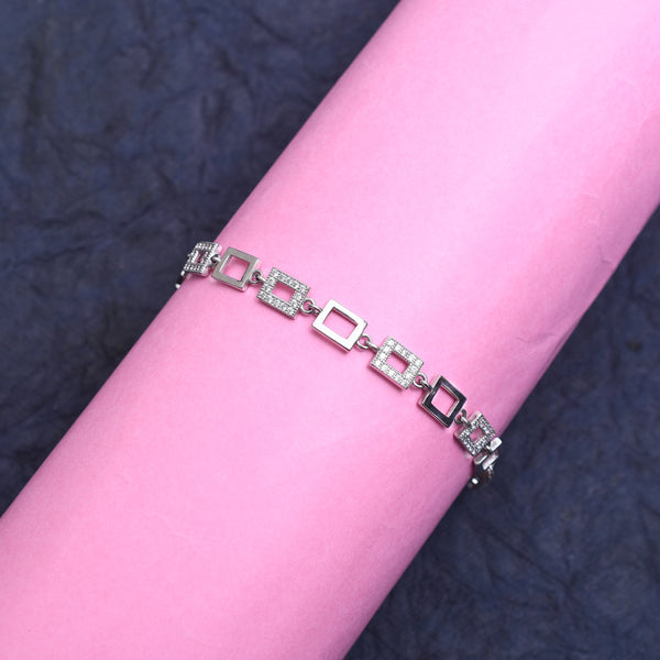 A silver bracelet with a sparkling canvas trail design, displayed on a pink cylindrical object.